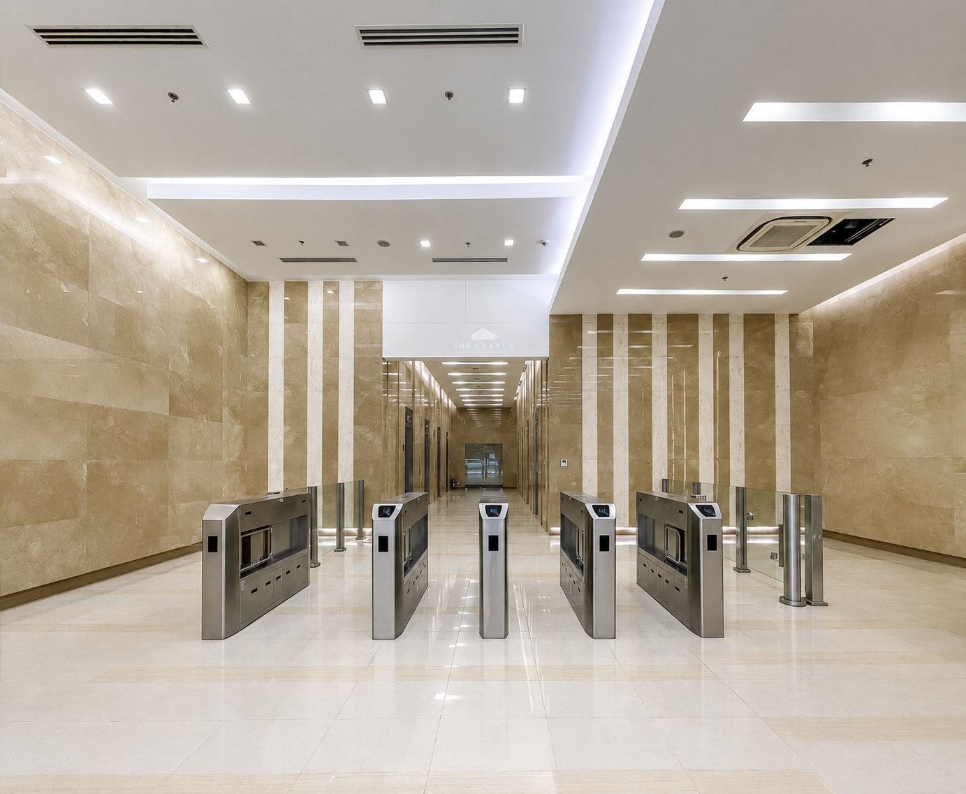 Wide view of a clean beige marble lobby with a row of stainless steel turnstiles at the entrance and a long hallway ahead.