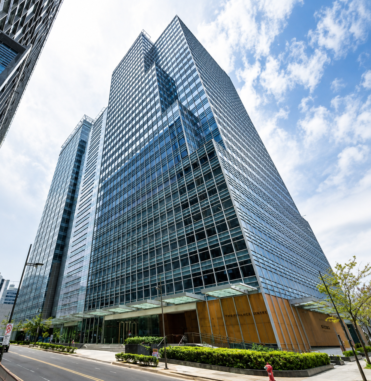 Tall glass-clad skyscraper with angular design, street-level entrance, and blue sky above.