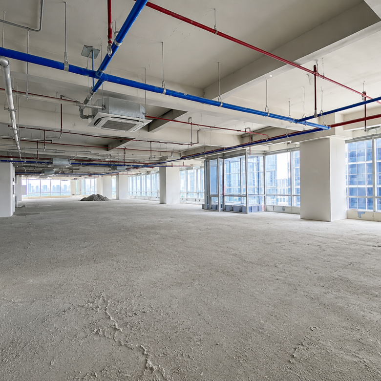 Empty unfinished office floor with exposed red and blue pipes, concrete floor, and large windows showing cityscape.
