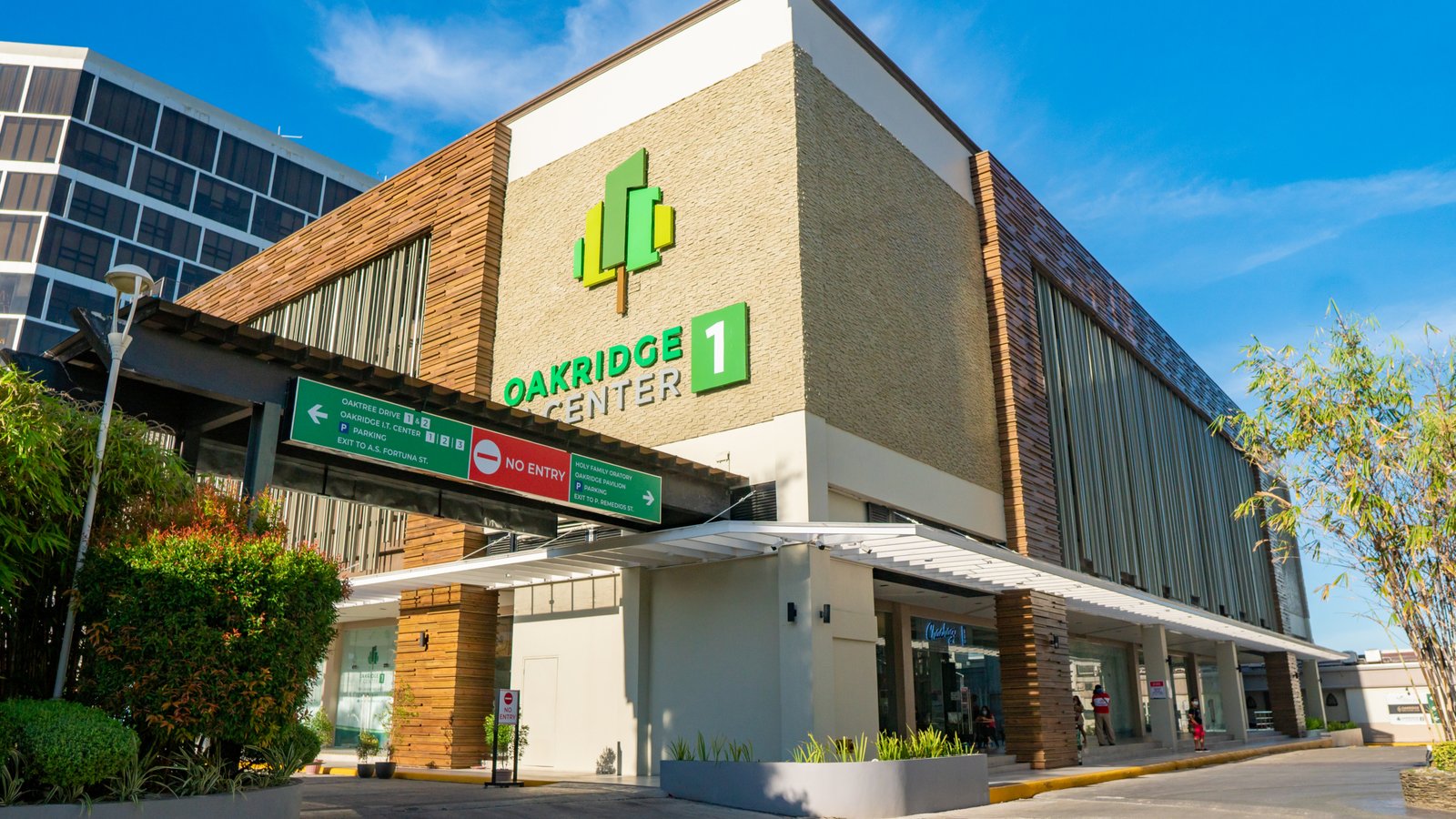 Exterior view of Oakridge Center shopping center with brick facade, green logo, and directional signs under a blue sky.