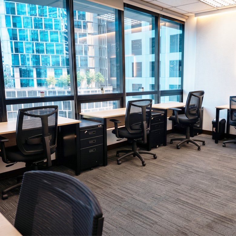 Row of workstations by large glass windows overlooking a city, with black mesh chairs and filing cabinets.