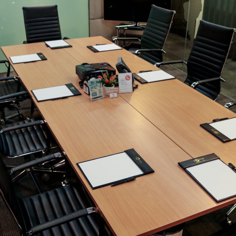 Large conference room with a wooden table and black ergonomic chairs around it; notepads and pens are set for a meeting.