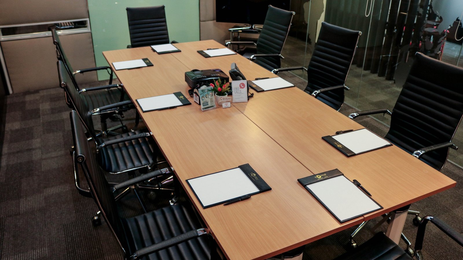 Large conference room with a wooden table and black ergonomic chairs around it; notepads and pens are set for a meeting.