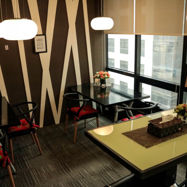 Cafe seating area with black tables, red floral cushions, and a bold black-and-white zigzag wall under white pendant lights.