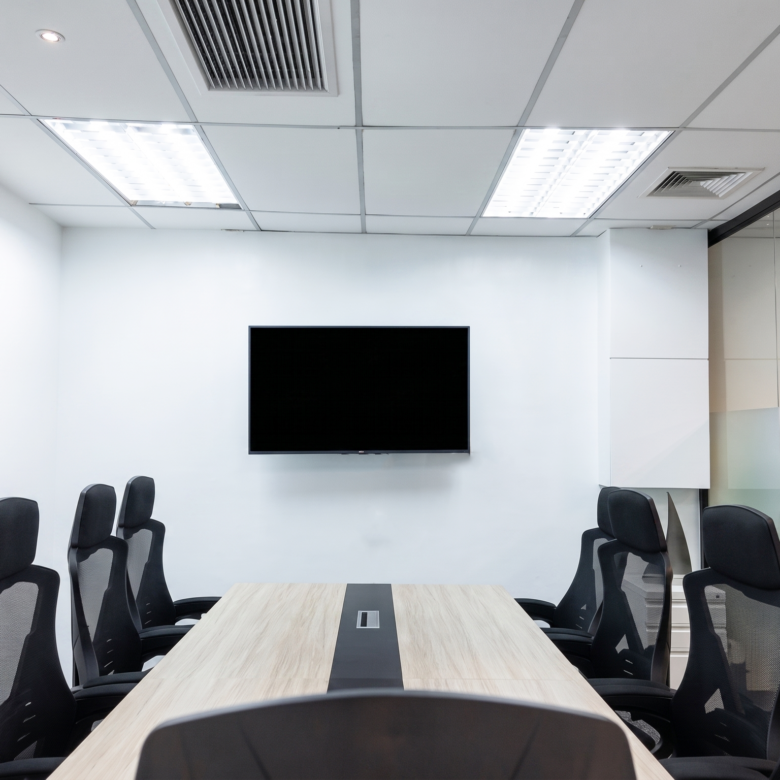 Conference room with a wall-mounted flat-screen TV, a long wood table, and black office chairs around it.