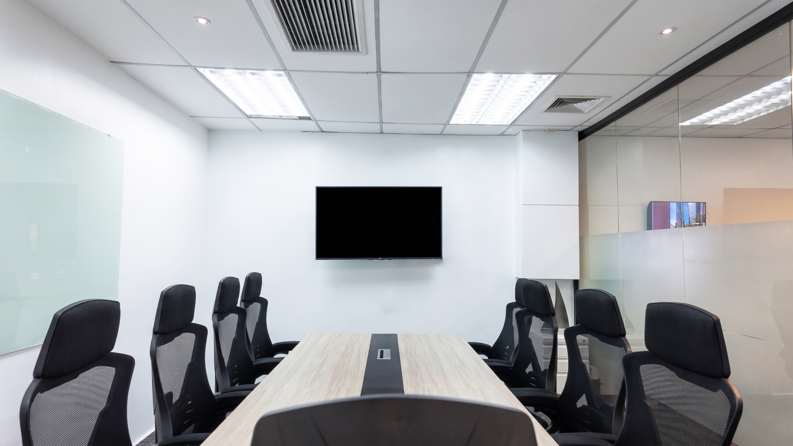 Meeting Room at Ortigas Conference room with a wall-mounted flat-screen TV, a long wood table, and black office chairs around it.