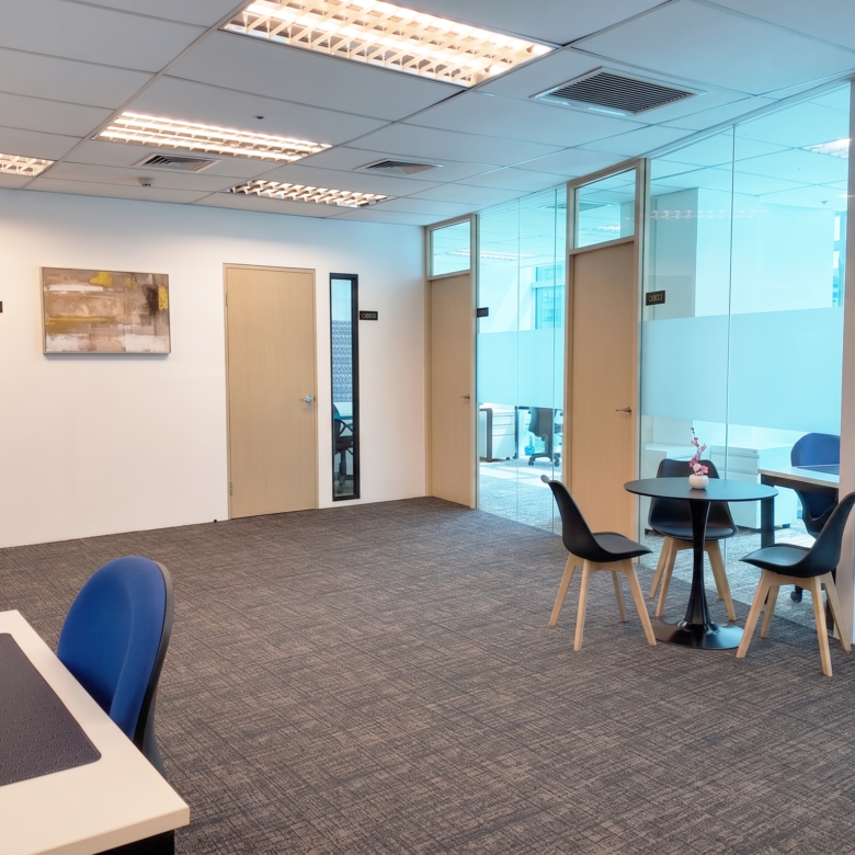 Modern open-plan office with glass-walled meeting rooms, light wood doors, and a seating area with blue chairs and tables.